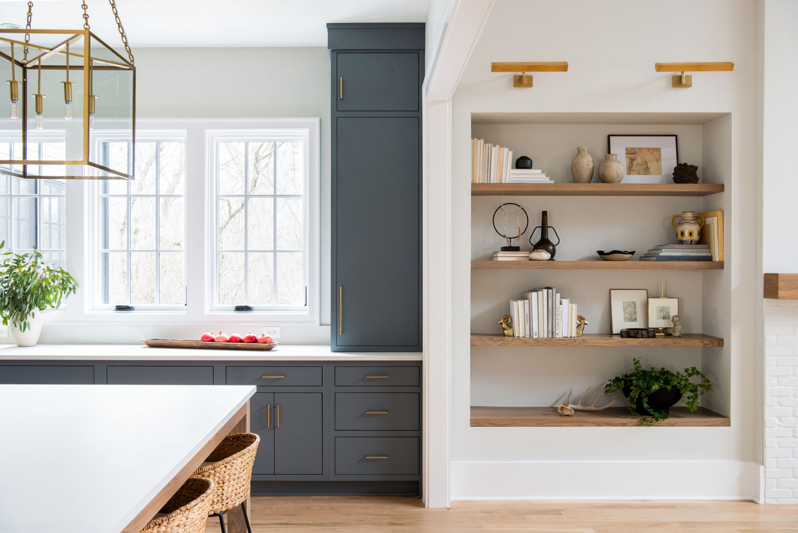 Kitchen with dark navy cabinets with upper windows and view of family room built-ins with natural wood shelving