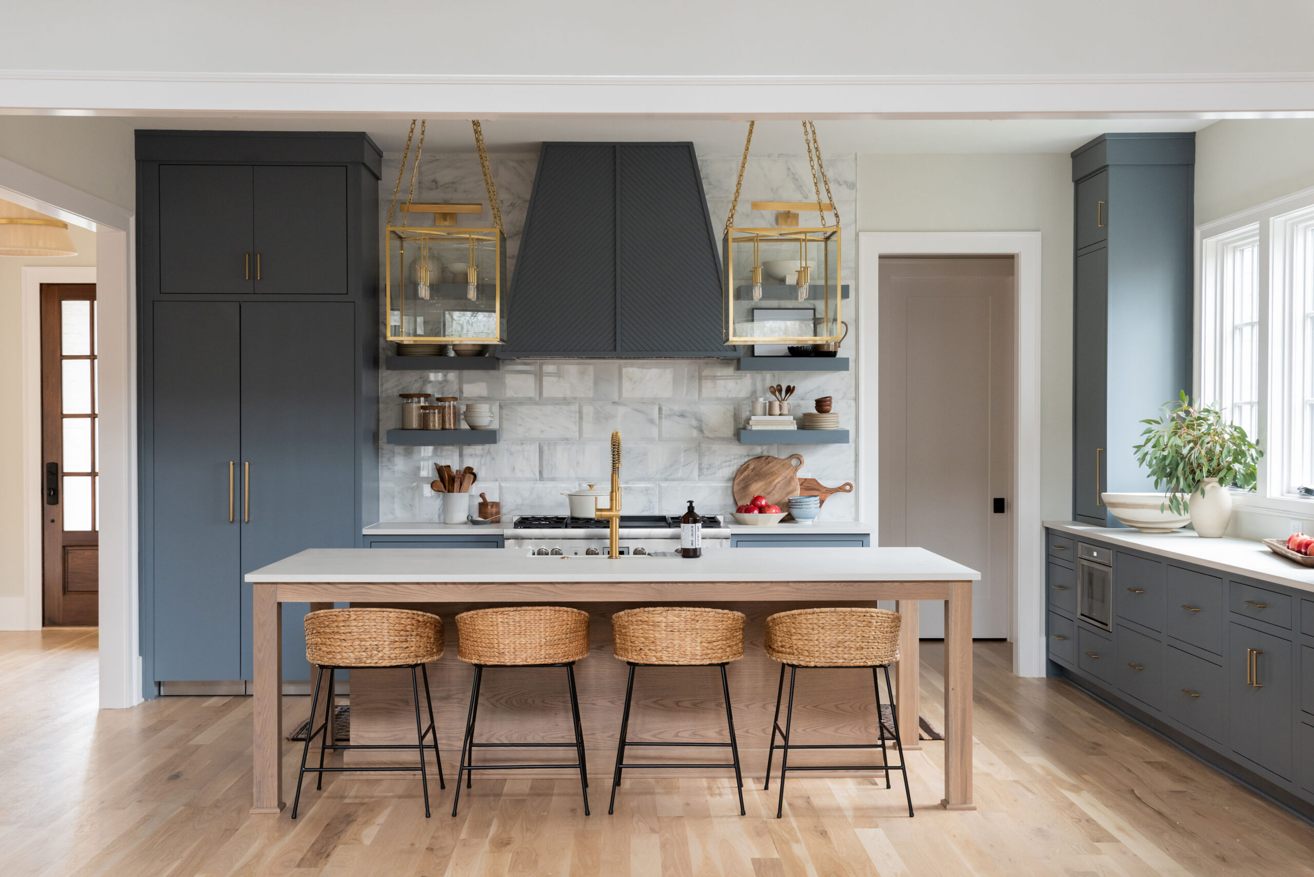 Kitchen with dark navy cabinets with marble tile backplash with gold lantern pendants and window light