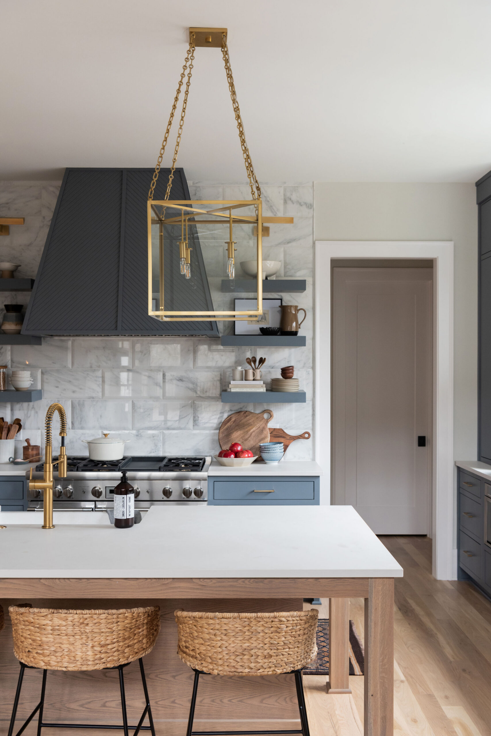 Kitchen with dark navy cabinets with marble tile backplash with gold lantern pendants and window light