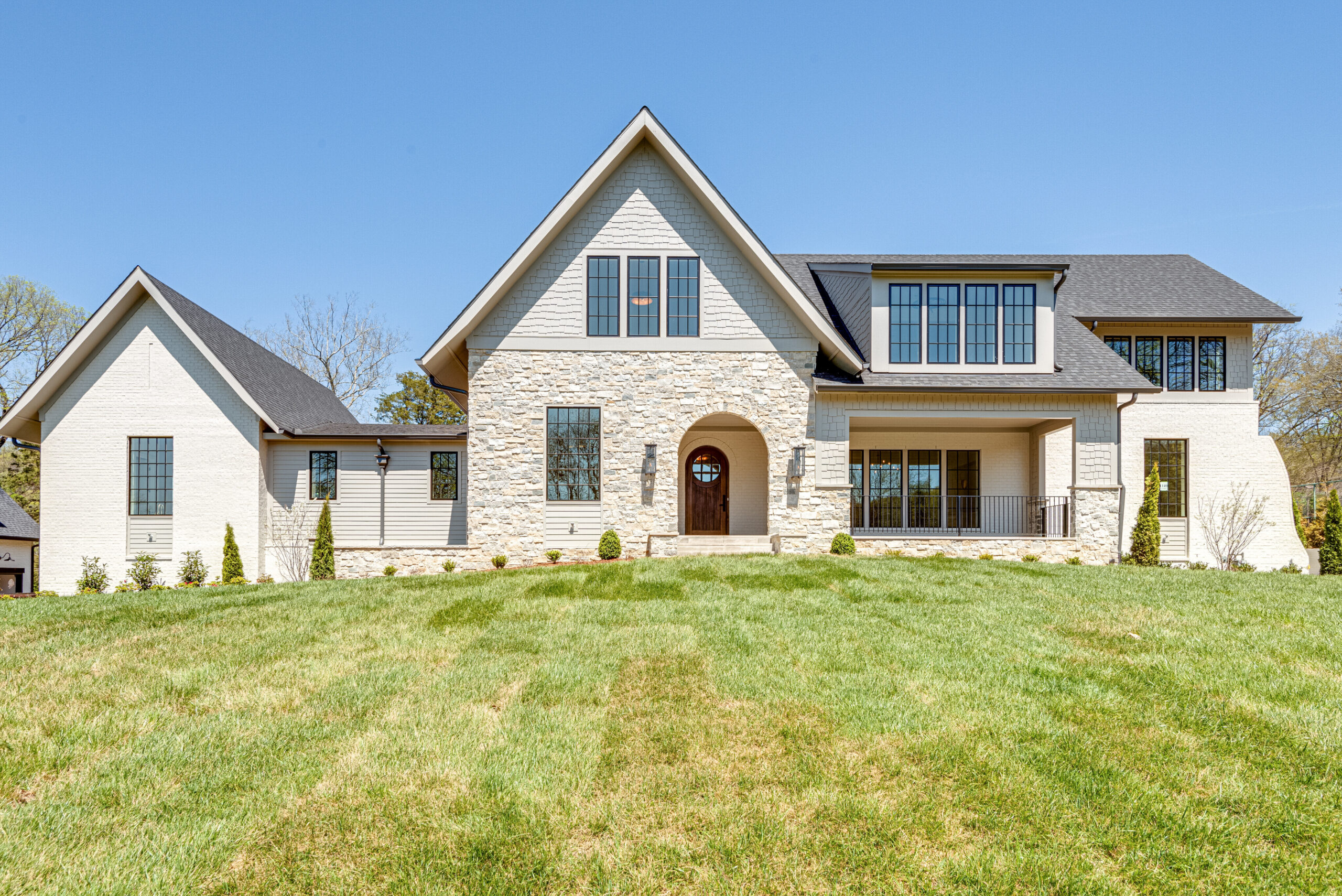 Stone faced two story home with front home entry with arched opening to patio leading to an arched wooden door