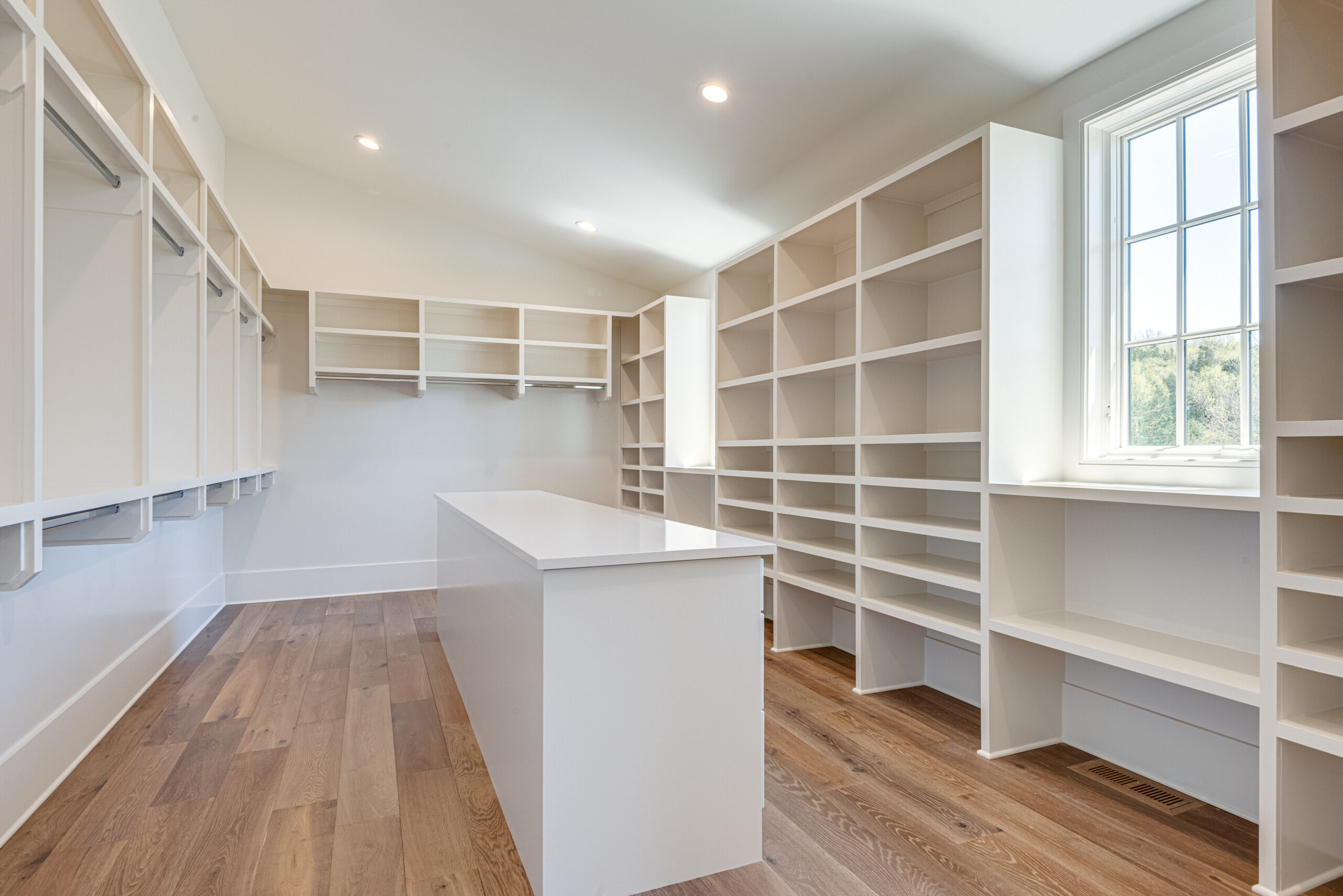 Large white walk-in closet with open shelving, and a center island with window light
