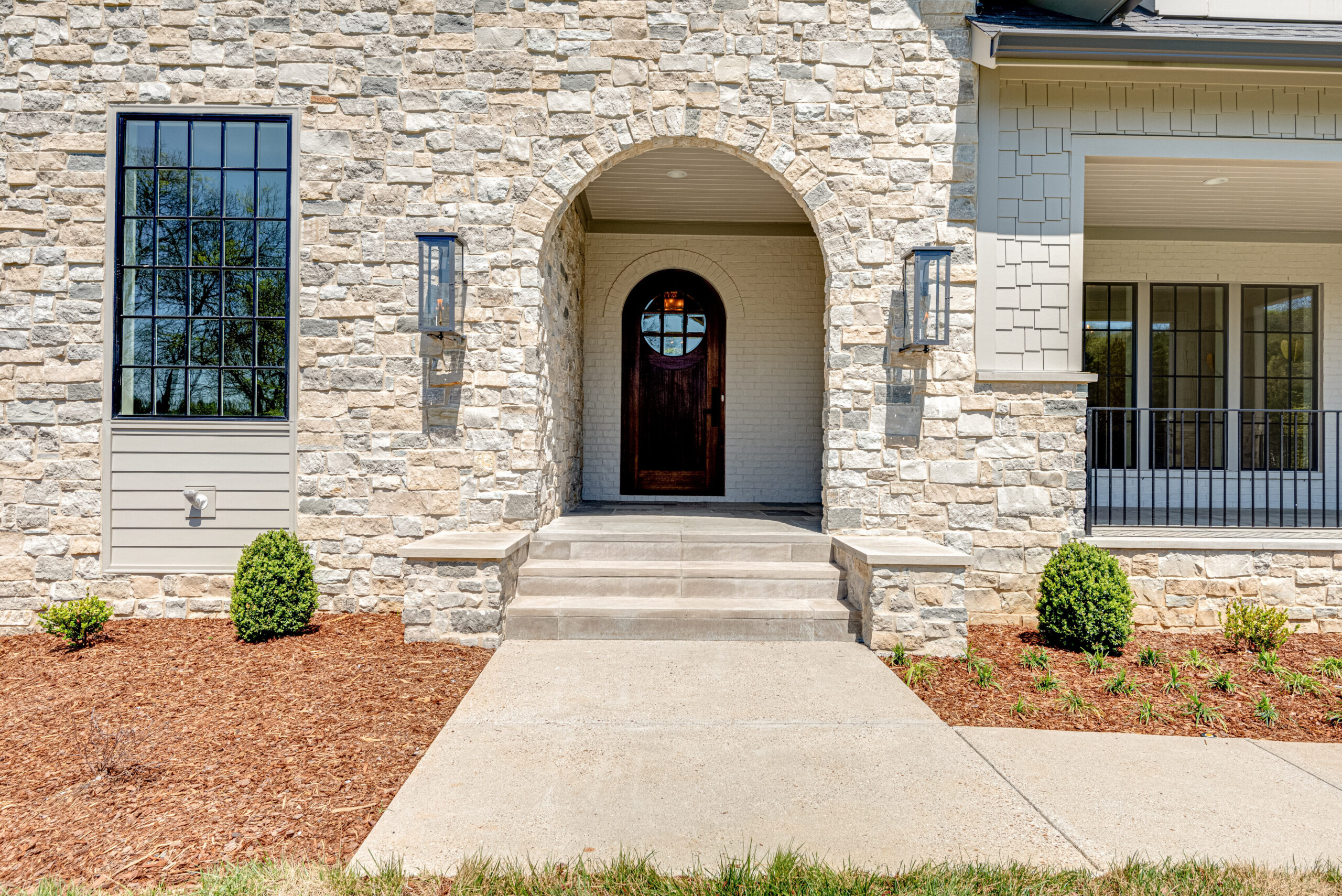 Stone faced front home entry with arched opening to patio leading to an arched wooden door