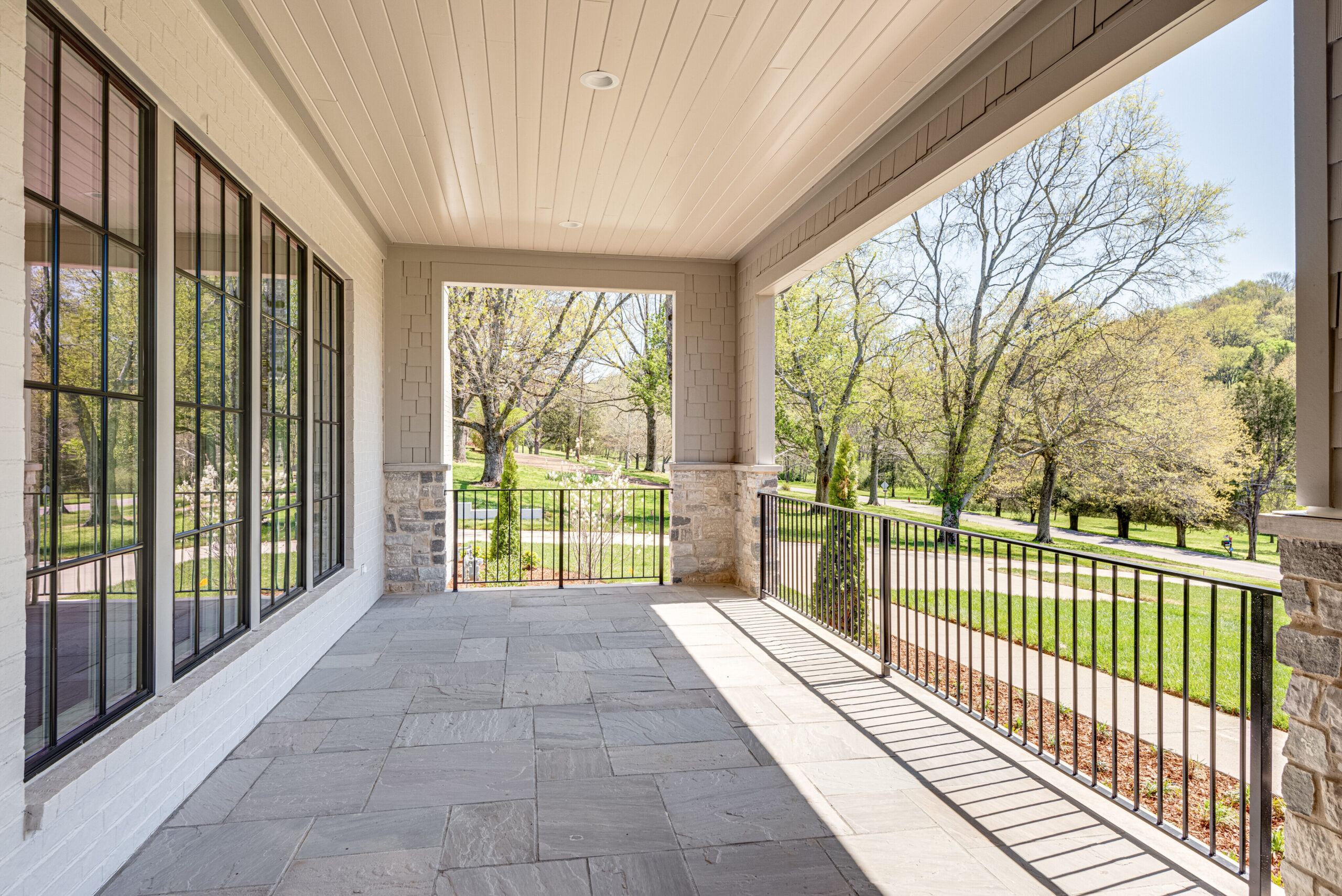 Front spacious patio of a cream home featuring black iron spindles and widows