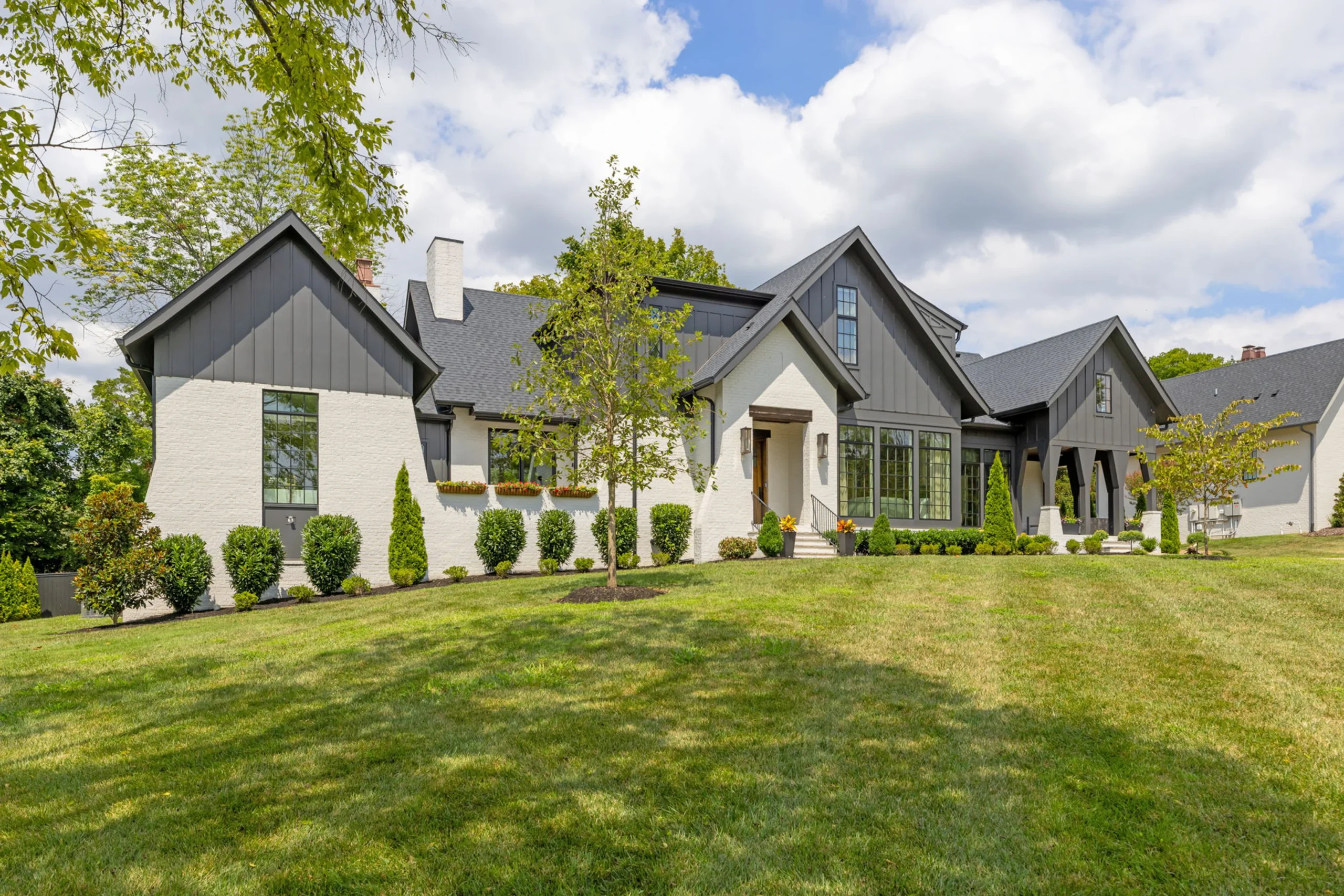 White brick and dark board-and-batten home exterior with gabled rooflines and a green lawn