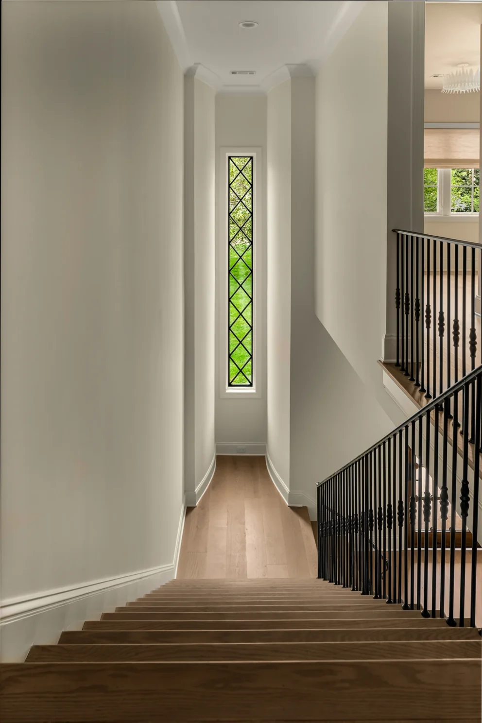 Staircase with a tall leaded-glass window, dark metal balusters, and wood treads