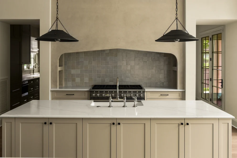 Kitchen with large island, two black dome pendants, and a stainless range in a gray zellige tile alcove