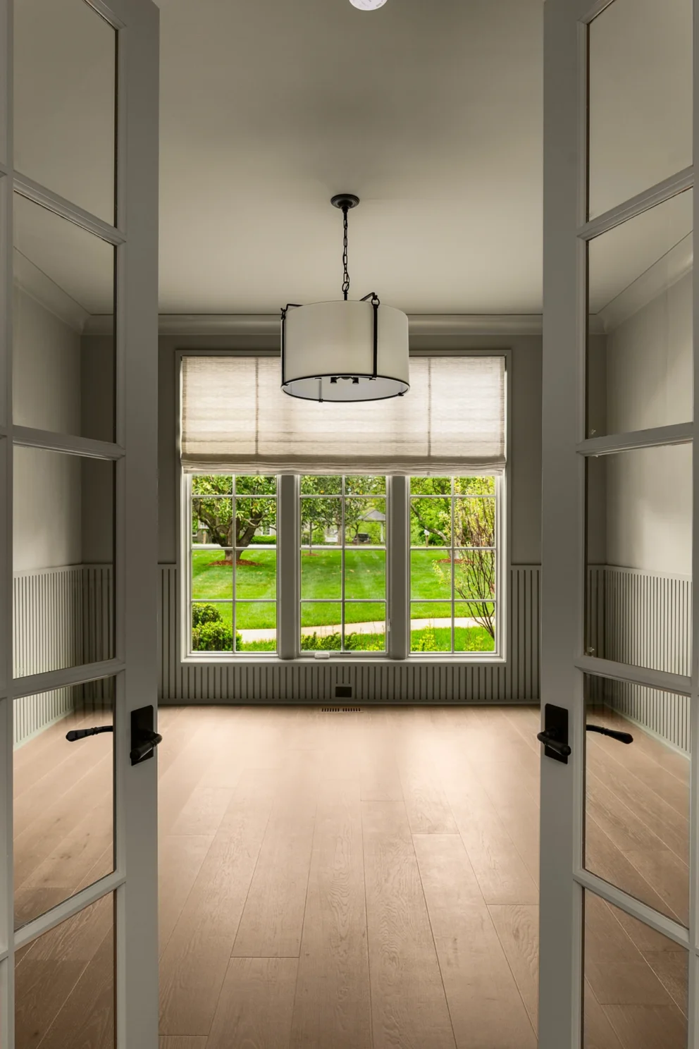 View through open double doors into a room with a window and a lantern pendant light