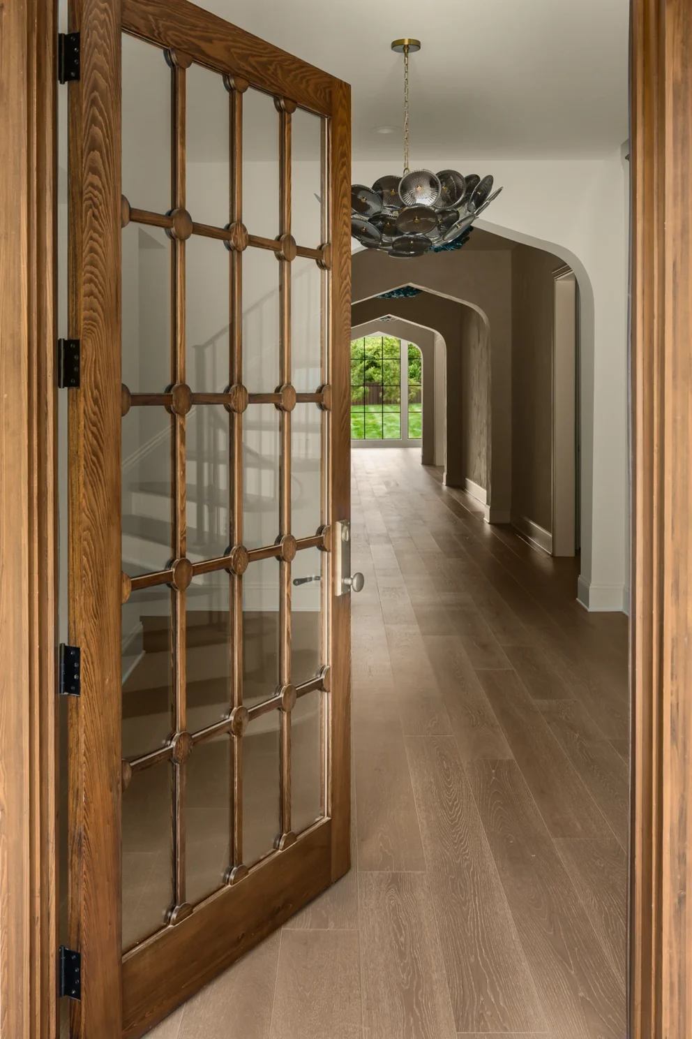 Open wood-framed glass door revealing a hallway with a dark floral disc chandelier