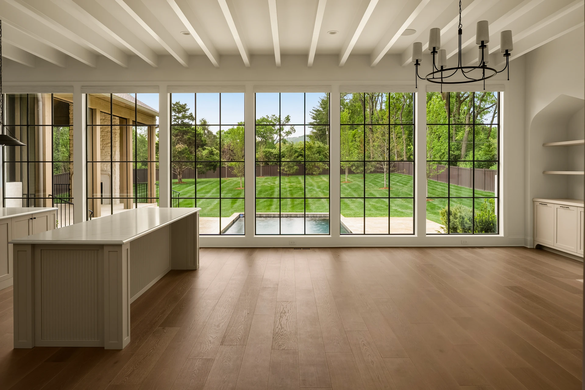Great room with a wall of windows overlooking the lawn and pool, and an iron chandelier