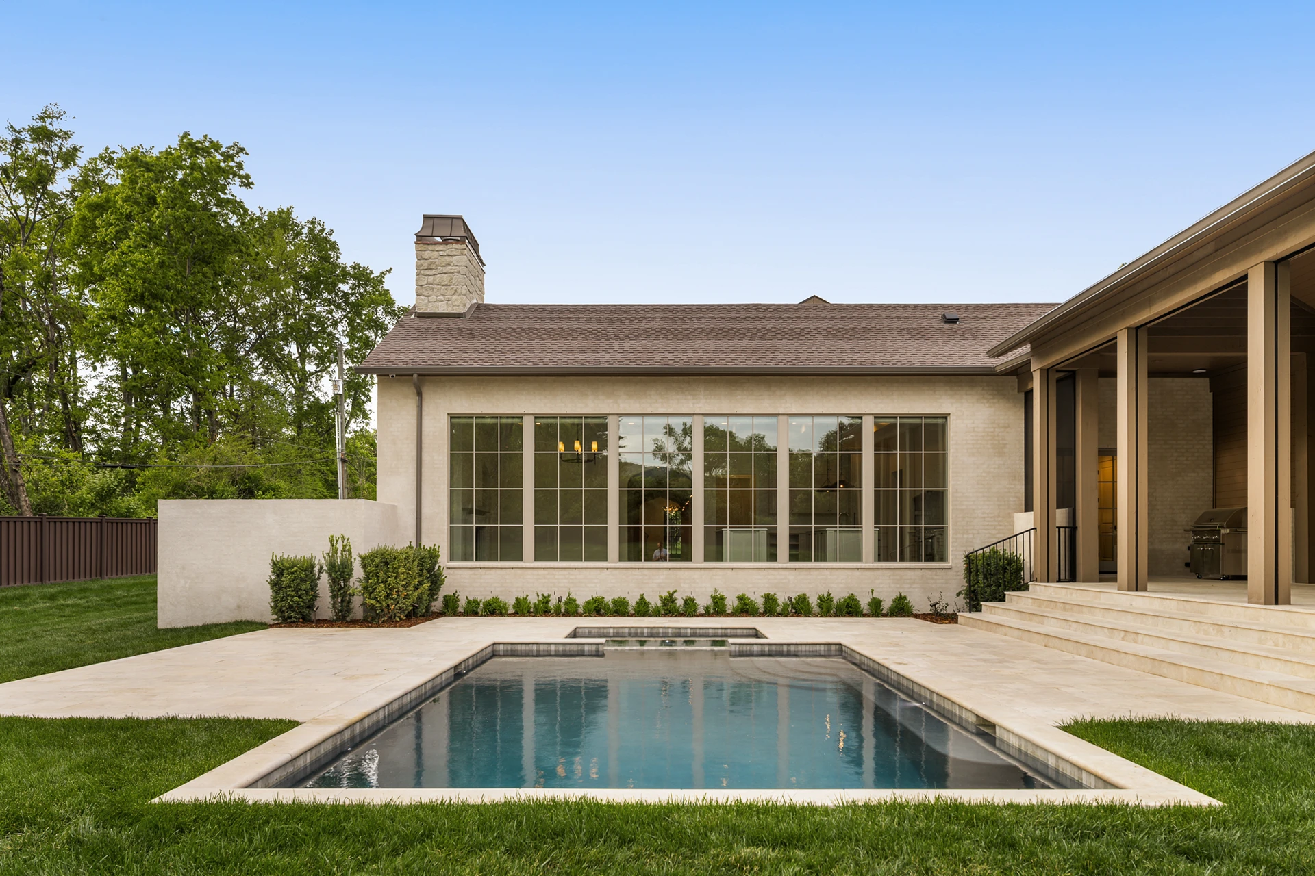 Backyard with in-ground pool and stone patio beside a single-story home with a wall of windows