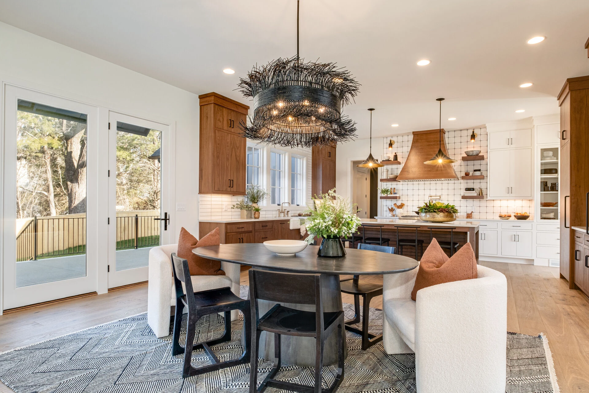 Dining area with round table, feathered twig chandelier, and a wood-and-white kitchen beyond