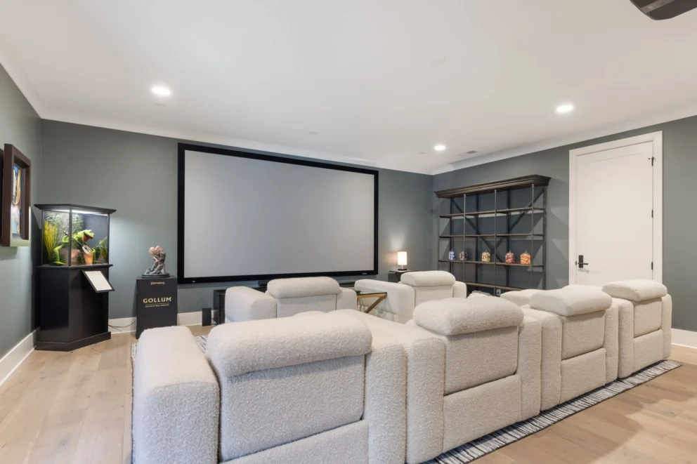 Home theater room with tiered cream recliners facing a projection screen and gray walls