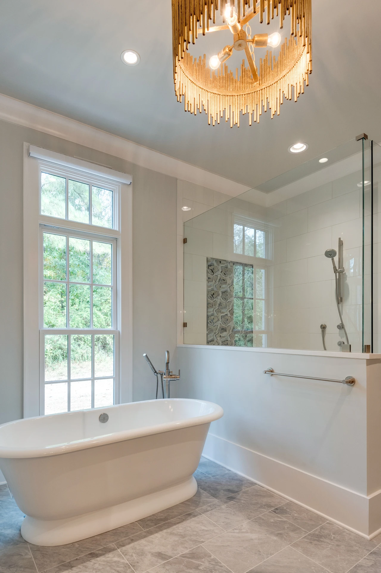 Master bath with freestanding tub, gold tiered chandelier, and a glass walk-in shower by a window