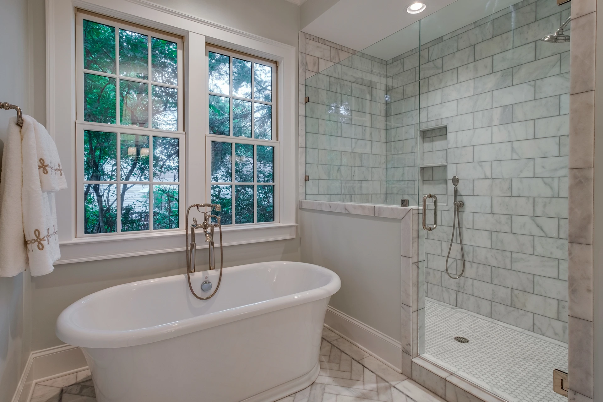 Master bath with freestanding tub under double windows and a marble glass walk-in shower