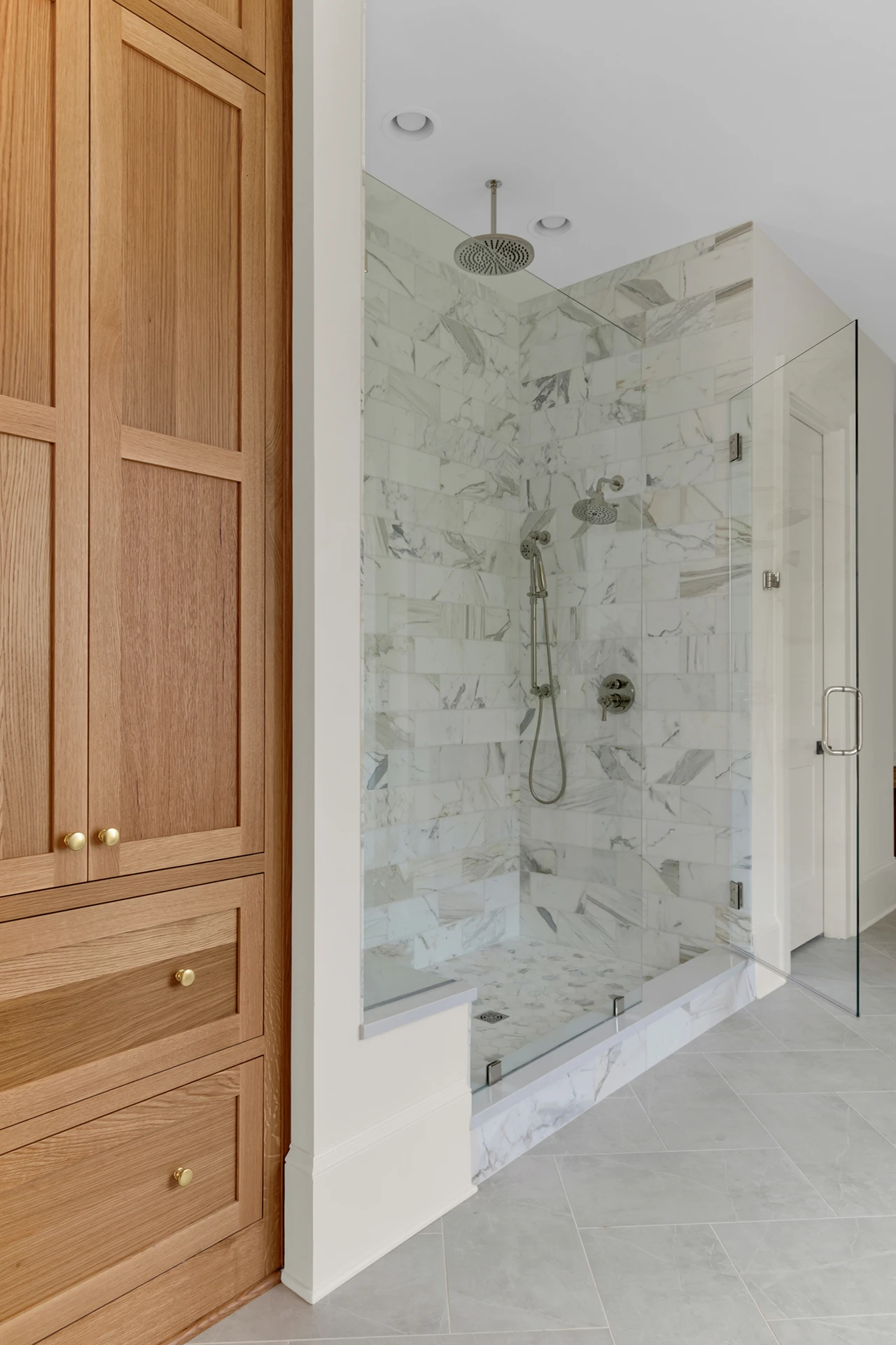 Master bath with wood linen cabinet and a marble walk-in shower with rainfall head