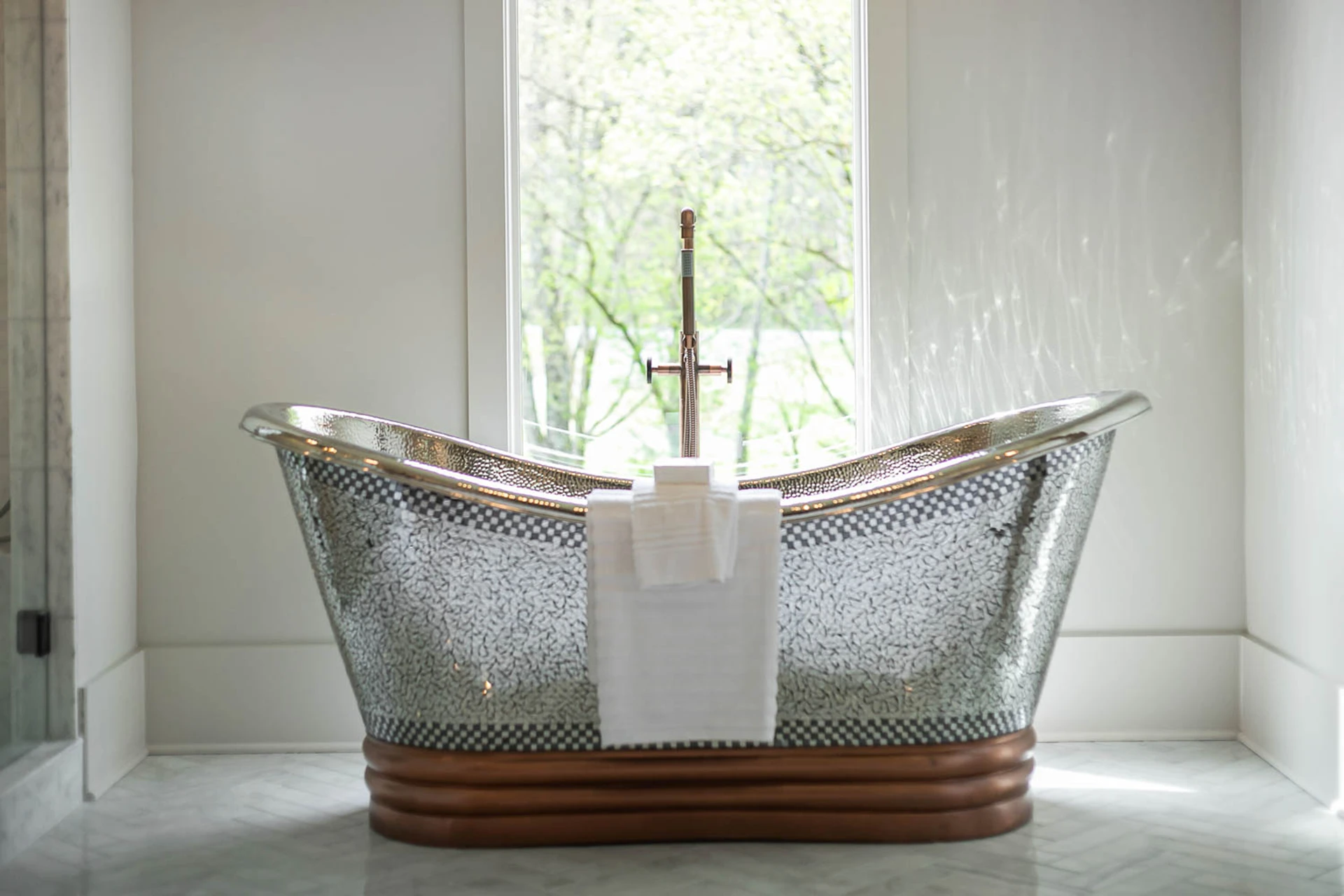 Metallic mosaic slipper tub in front of a window with a white towel draped over the side