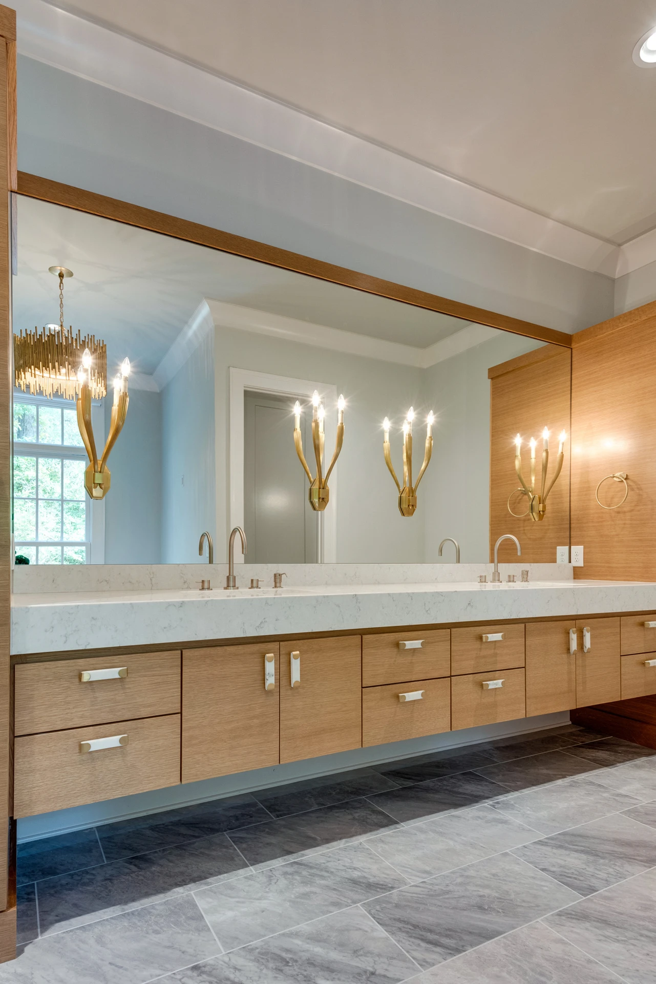 Master bath with wood floating dual vanity, large mirror, gold branch sconces, and gray marble floor