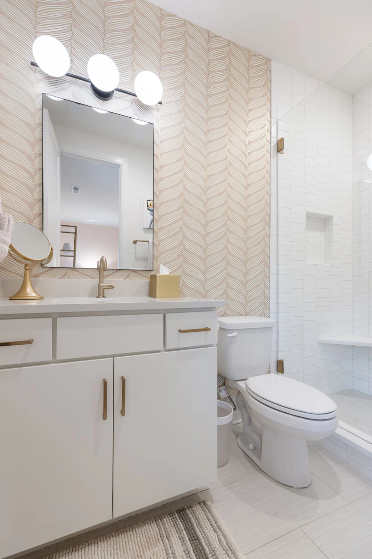 Bathroom with white vanity, herringbone wallpaper, round three-globe light, and a tub-shower combo