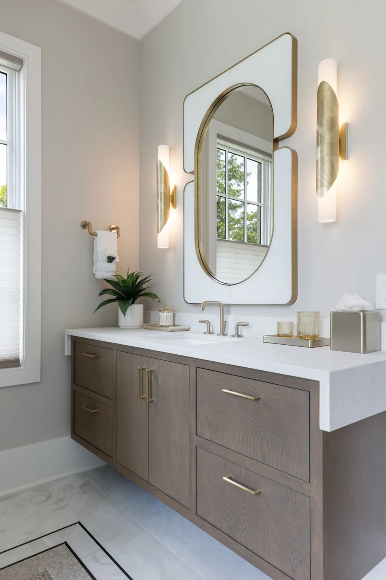 Bathroom with wood double vanity, gold rounded-square mirror, gold sconces, and a window
