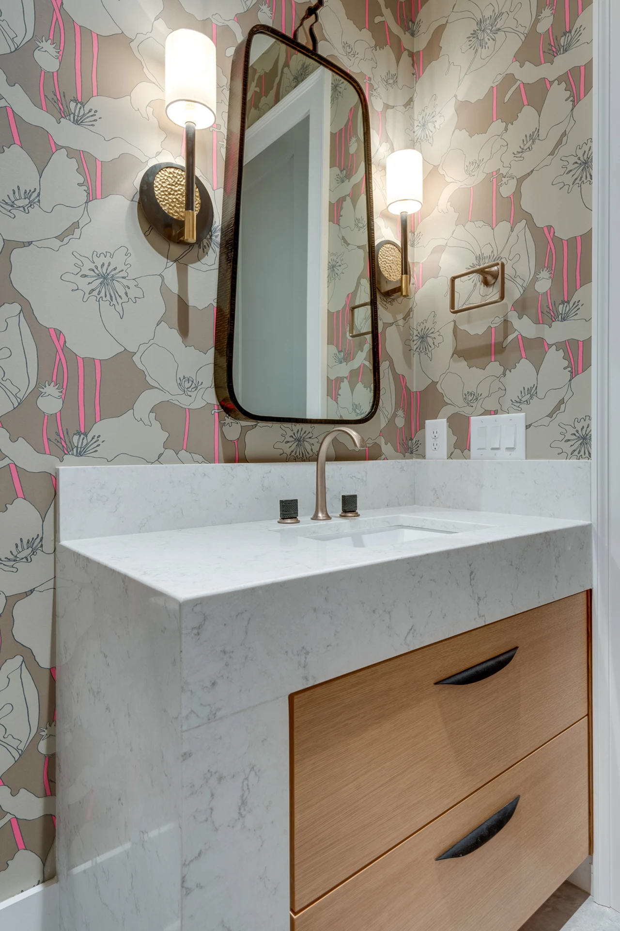 Powder room with floral wallpaper, wood vanity, marble waterfall counter, and an arched mirror