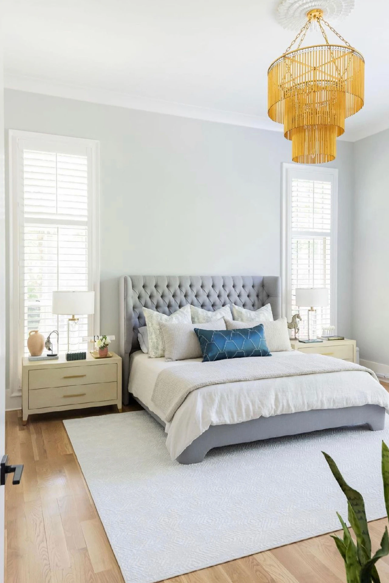 Bedroom with light gray walls, tufted gray headboard, and an amber tiered chandelier