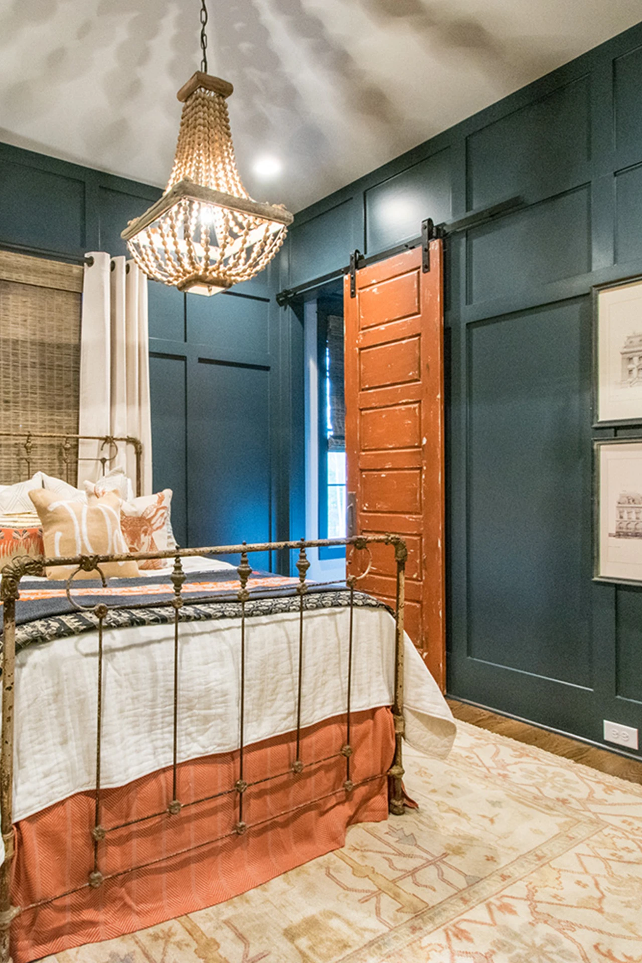 Bedroom with dark teal board-and-batten walls, iron bed, beaded chandelier, and a barn door