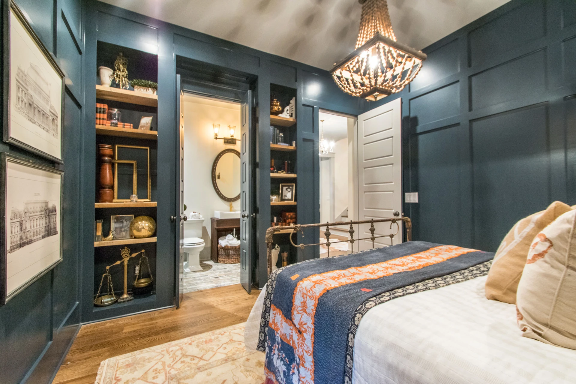 Navy board-and-batten bedroom with iron bed, beaded chandelier, and built-in shelving with an ensuite beyond