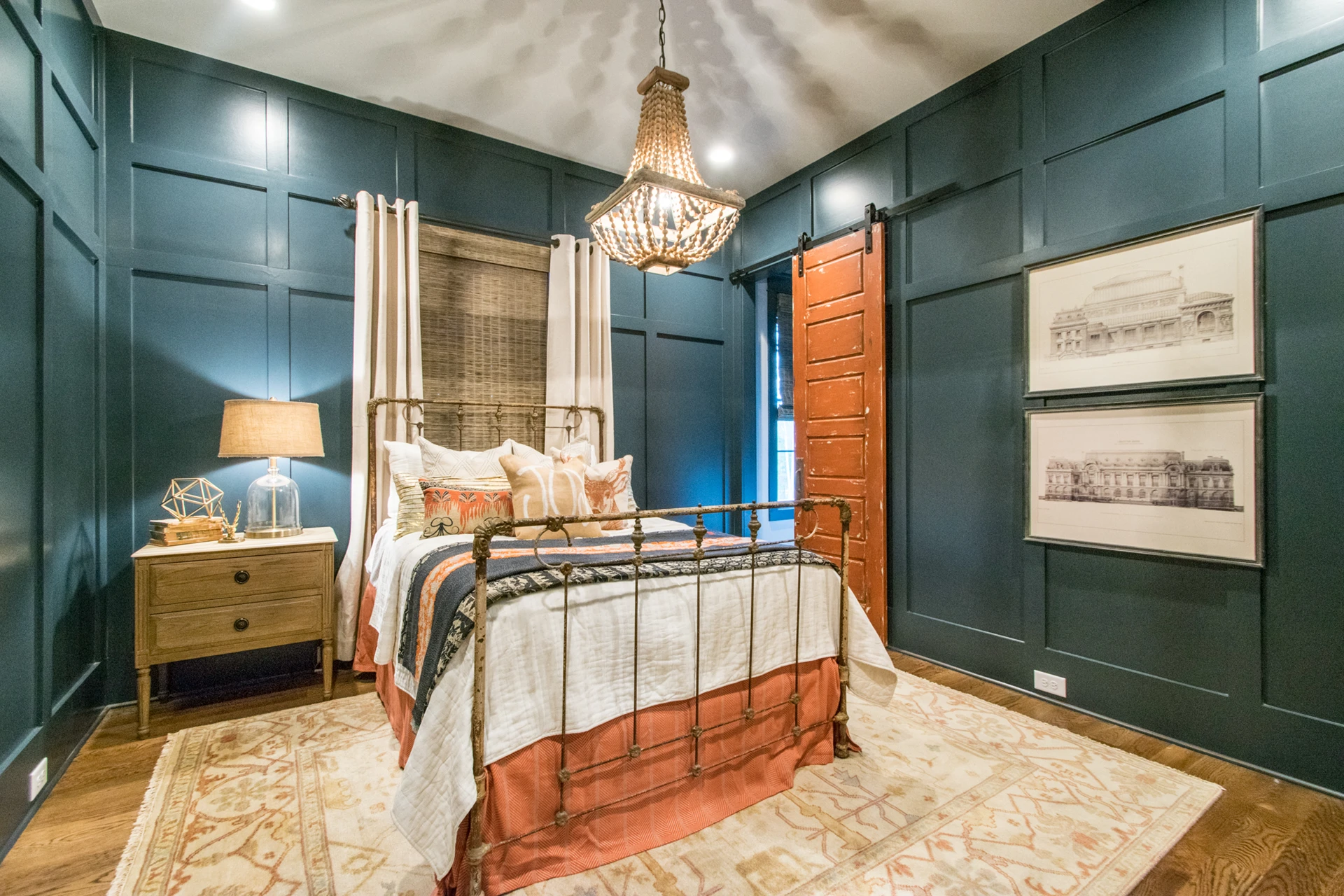 Bedroom with dark teal board-and-batten walls, iron canopy bed, beaded chandelier, and a barn door