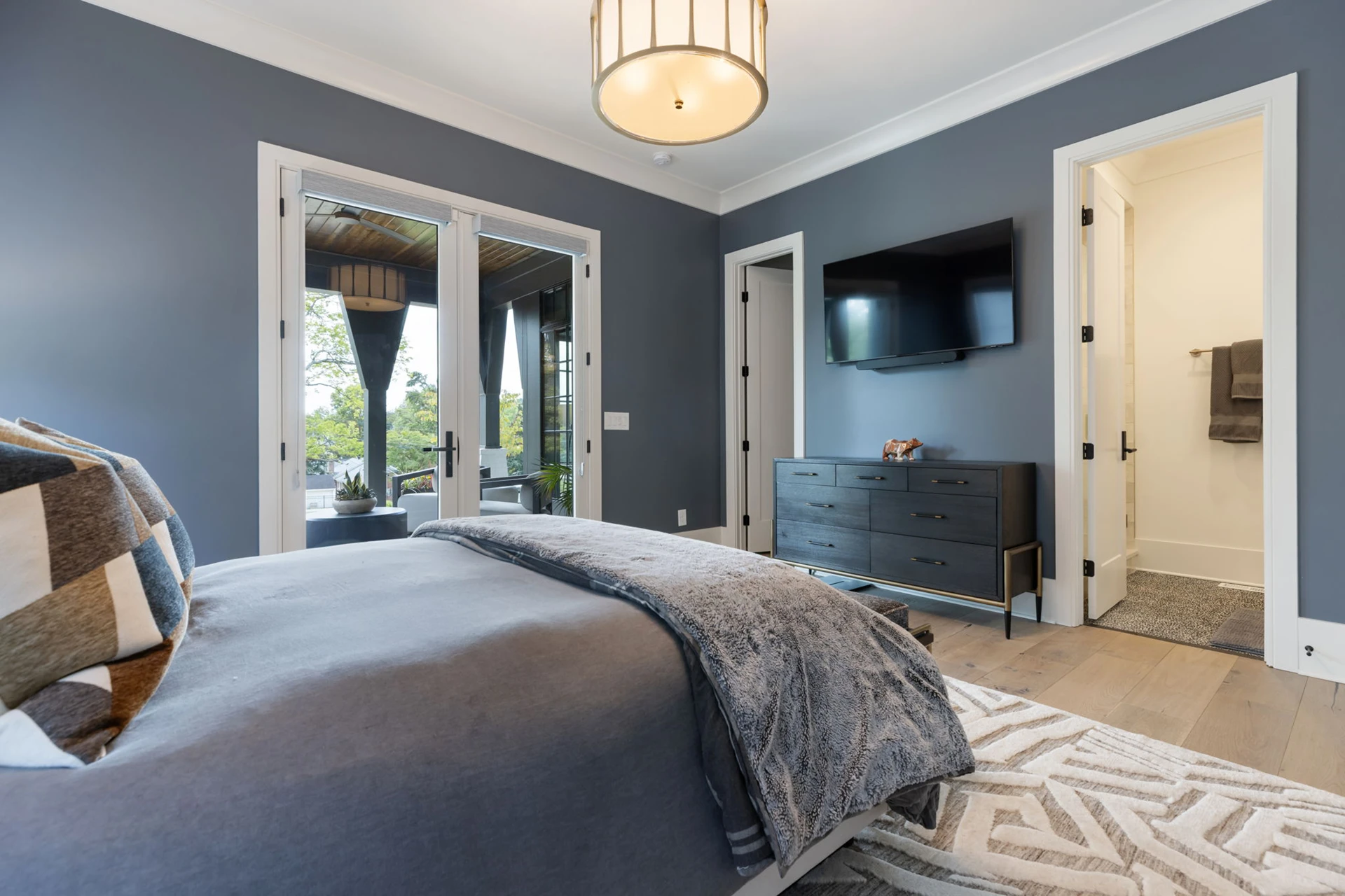 Bedroom with blue-gray walls, blue bedding, drum pendant, wall-mounted TV over a dresser, and French doors
