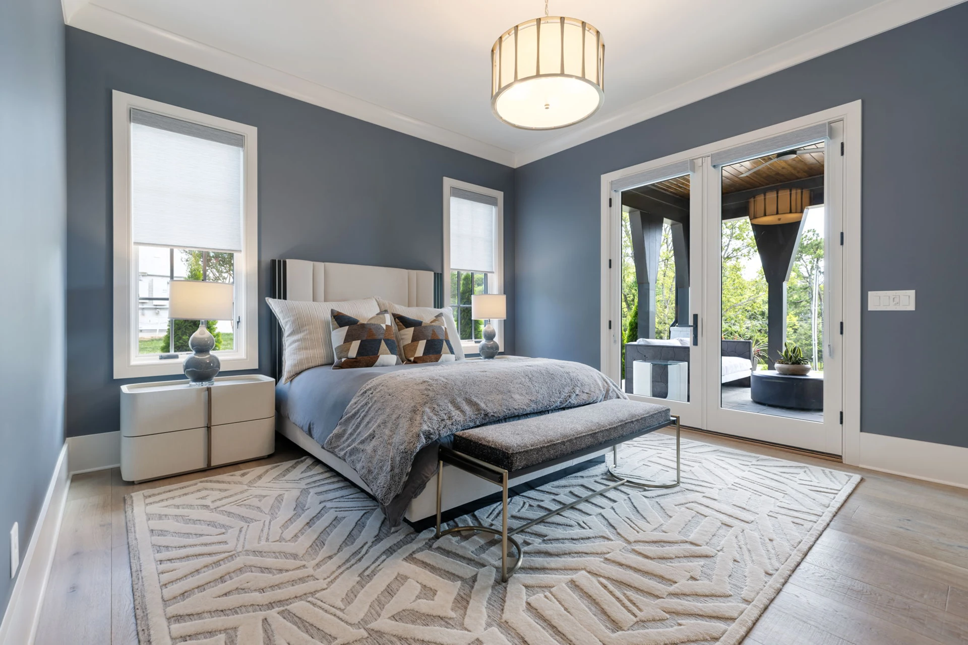 Bedroom with blue-gray walls, upholstered bed, drum pendant, and French doors to a porch