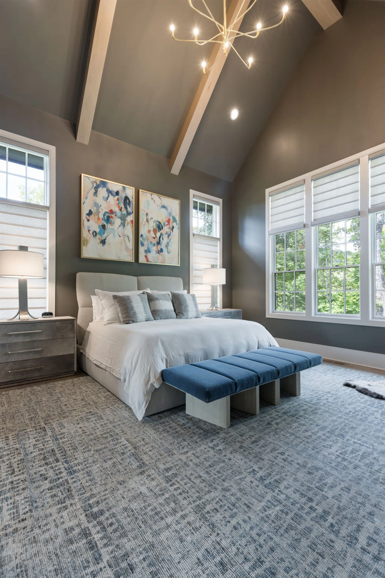 Bedroom with vaulted beamed ceiling, gray walls, upholstered bed, plantation shutters, and blue benches