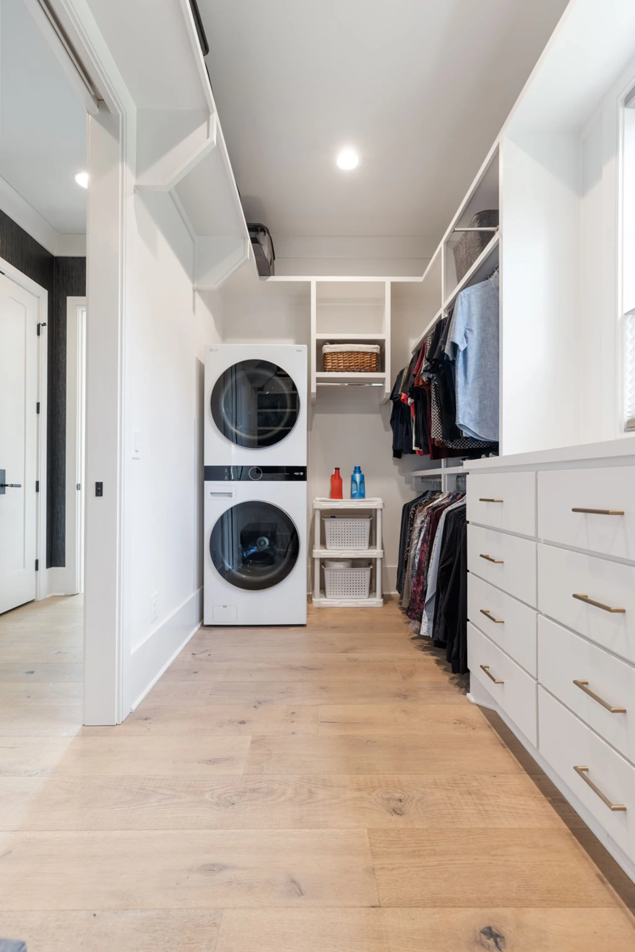 Walk-in closet with stackable washer and dryer, hanging clothes, and white drawers