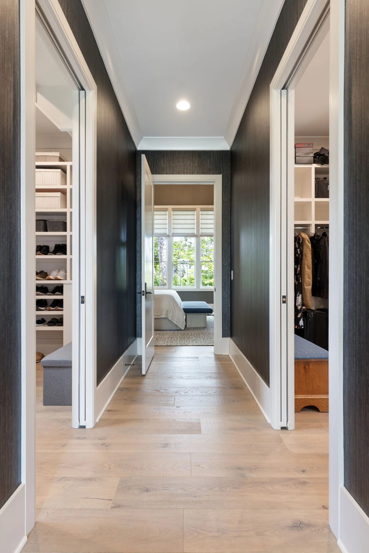 Dark-walled closet hallway with white built-in shelving on both sides and a view to a bedroom