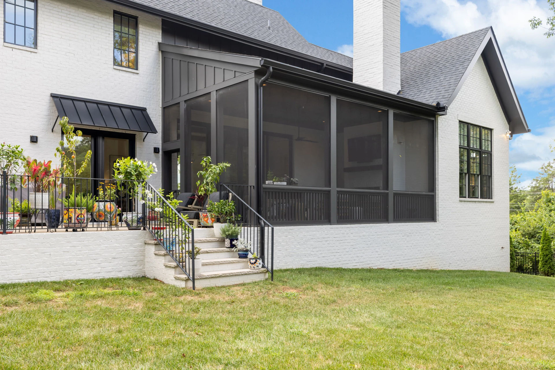 Rear exterior of a white brick home with screened porch, black metal awning, and deck steps