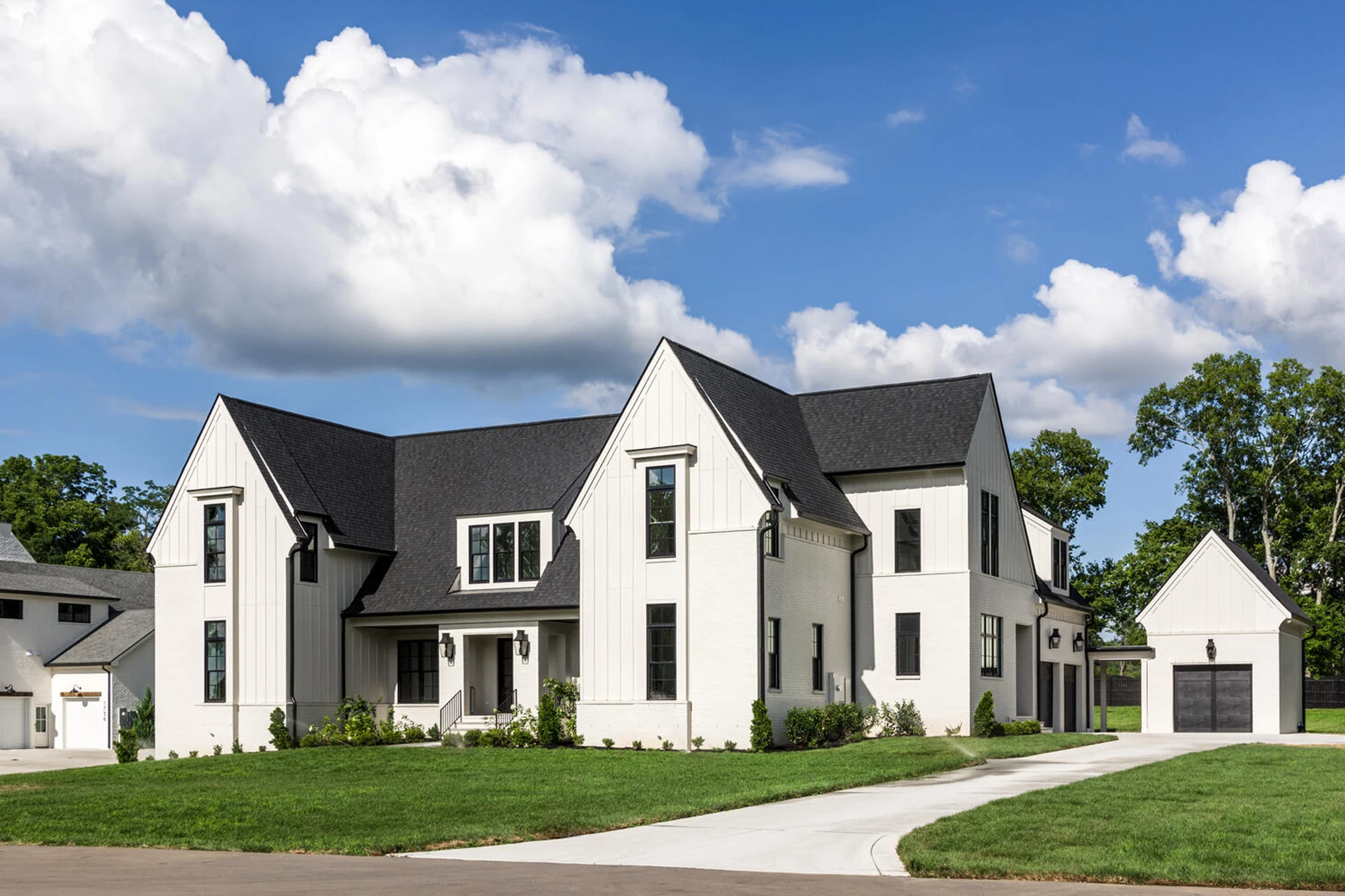 Large white two-story modern farmhouse with black roof and shutters, detached garage, and driveway