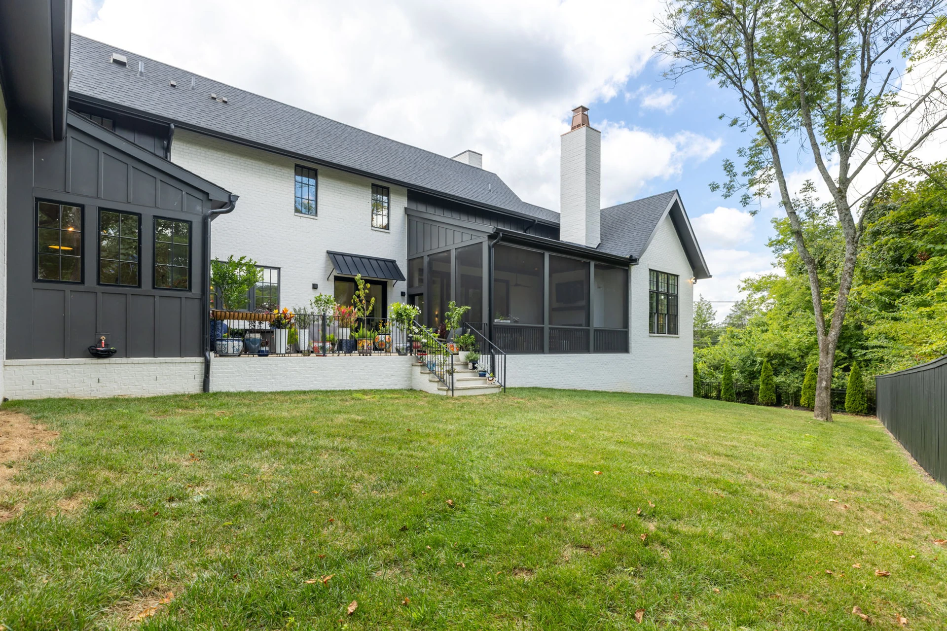 Rear exterior of a white and dark gray home with a screened porch, chimney, and green lawn