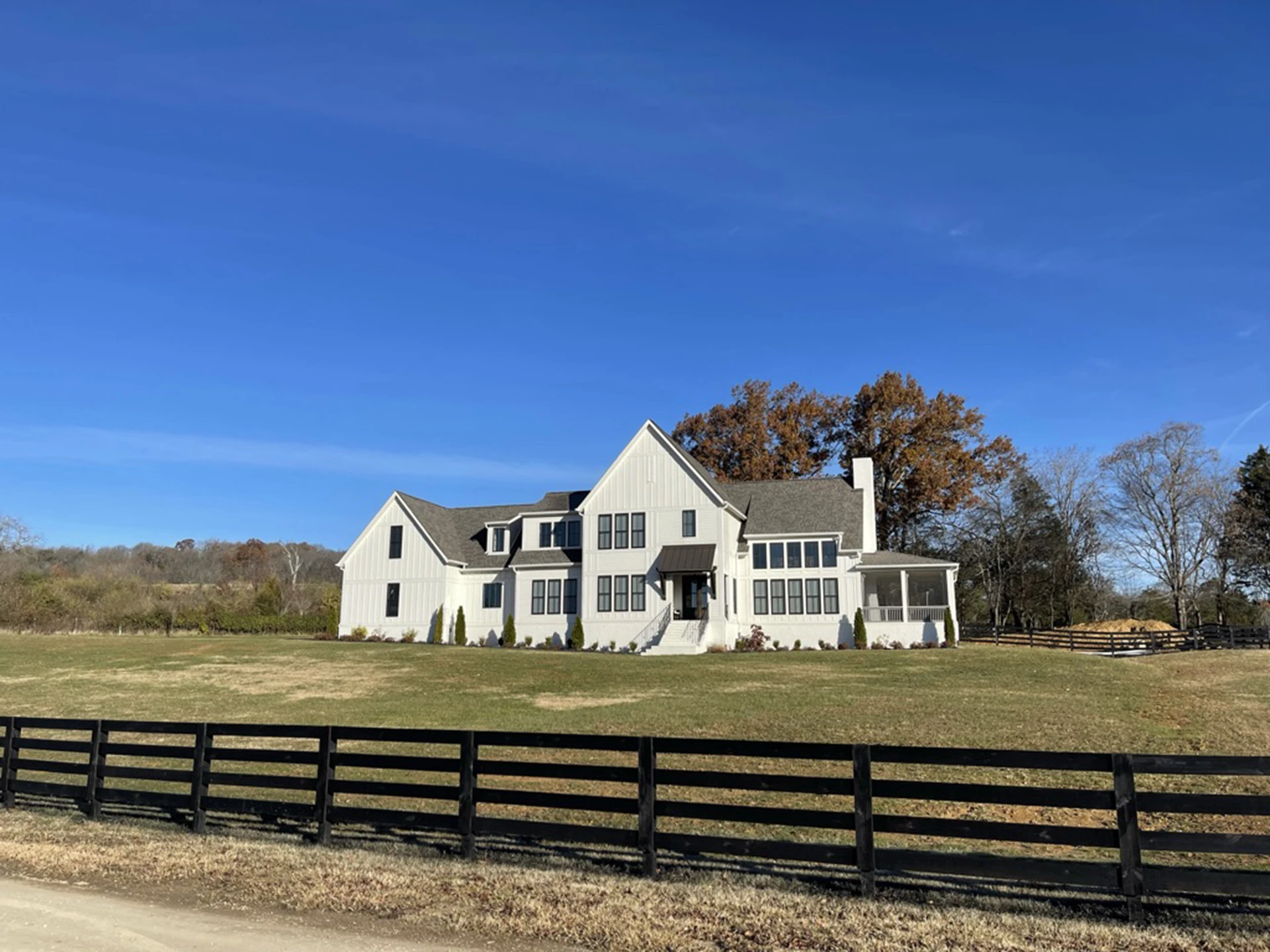 White two-story farmhouse behind a black wood fence in an open field under a clear blue sky