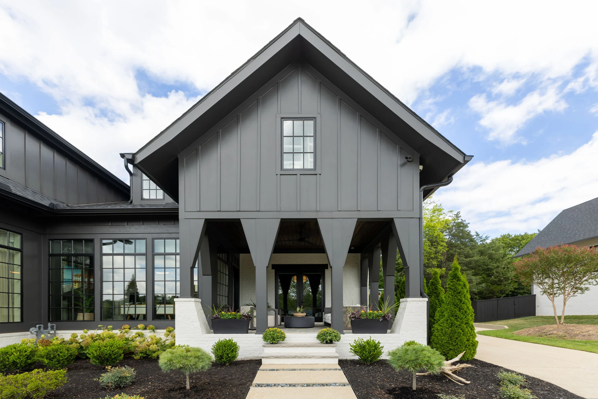 Dark gray board-and-batten home facade with a two-story columned entry porch and landscaped walkway