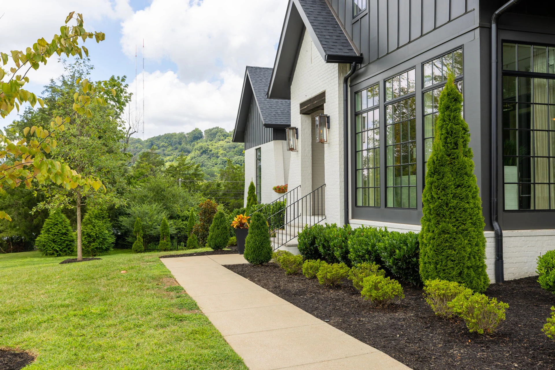 Angled view of a dark gray and white home with black-grid windows, walkway, and hills behind