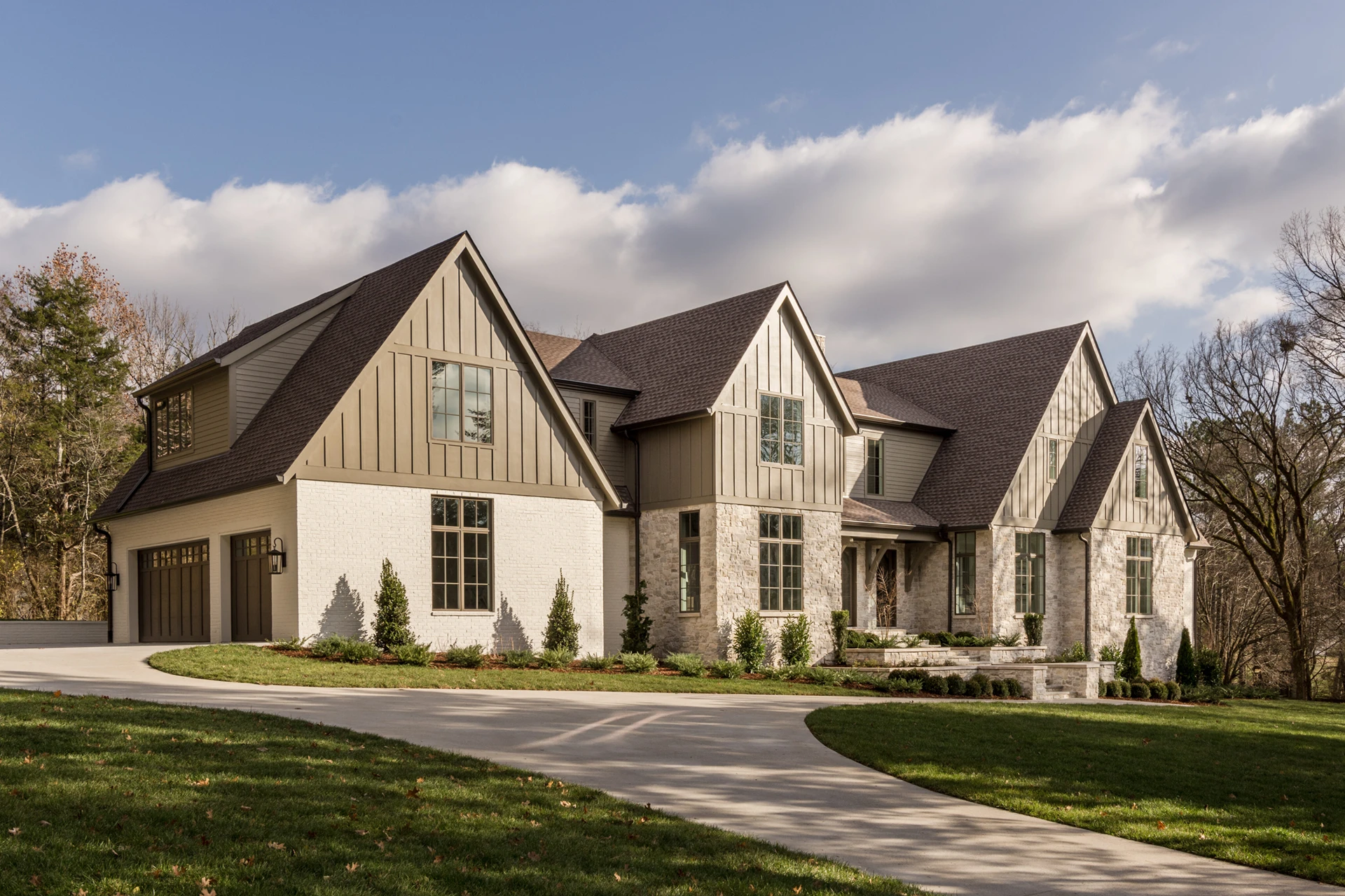 Two-story white brick and board-and-batten home with attached garage and a curved driveway
