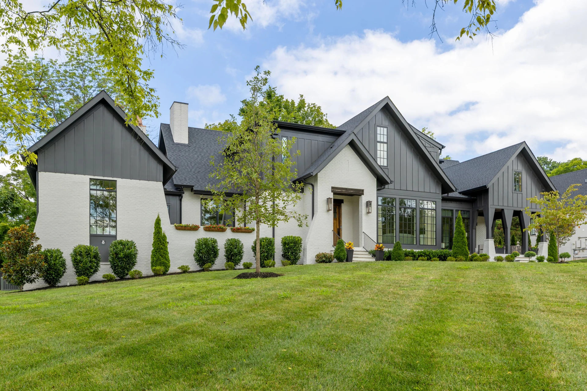 White brick and dark board-and-batten single-story home with dark roof and a manicured lawn
