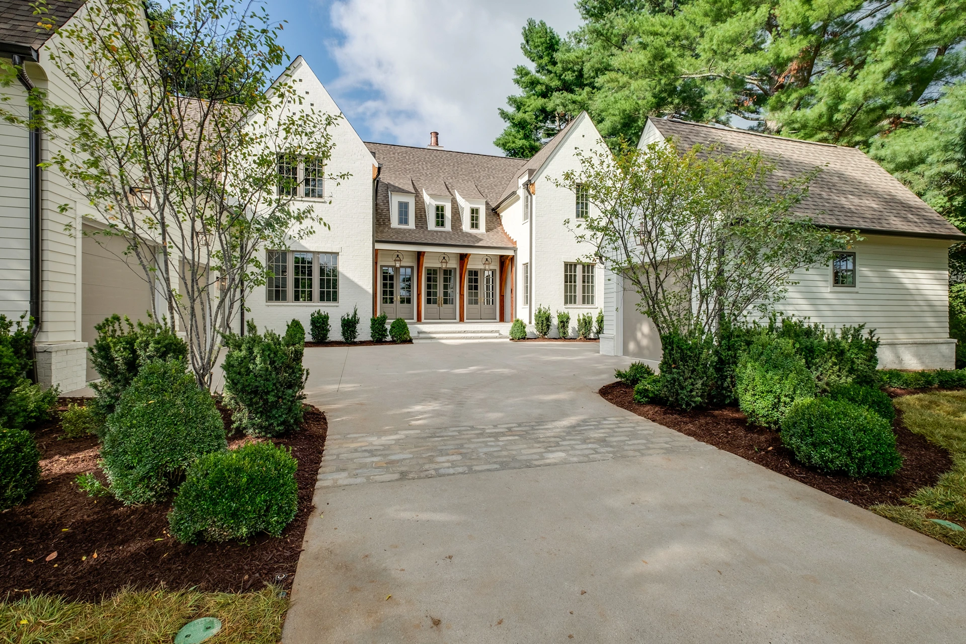 White two-story home with dormer windows, wood double doors, symmetrical wings, and a paver driveway