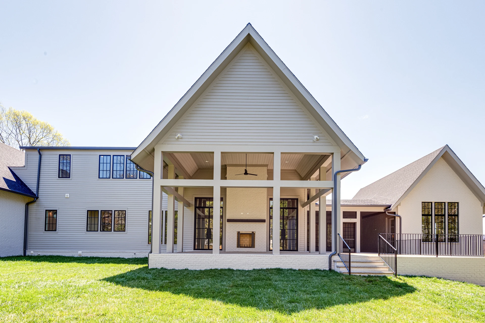 Rear exterior of a cream home with a large covered porch under a tall gable and black-grid windows