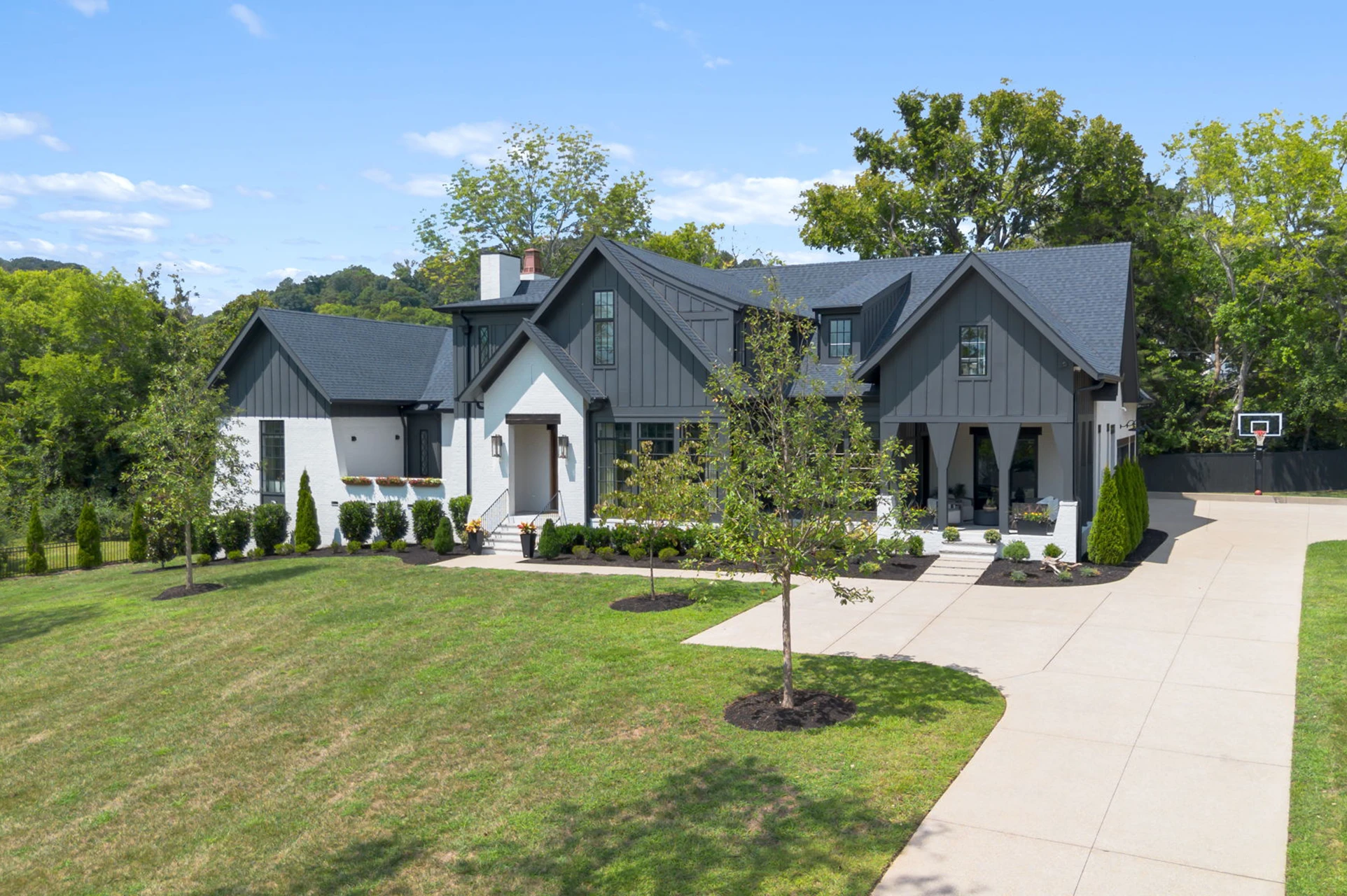 Elevated view of a white and gray modern farmhouse with black roof, multiple gables, and a landscaped yard
