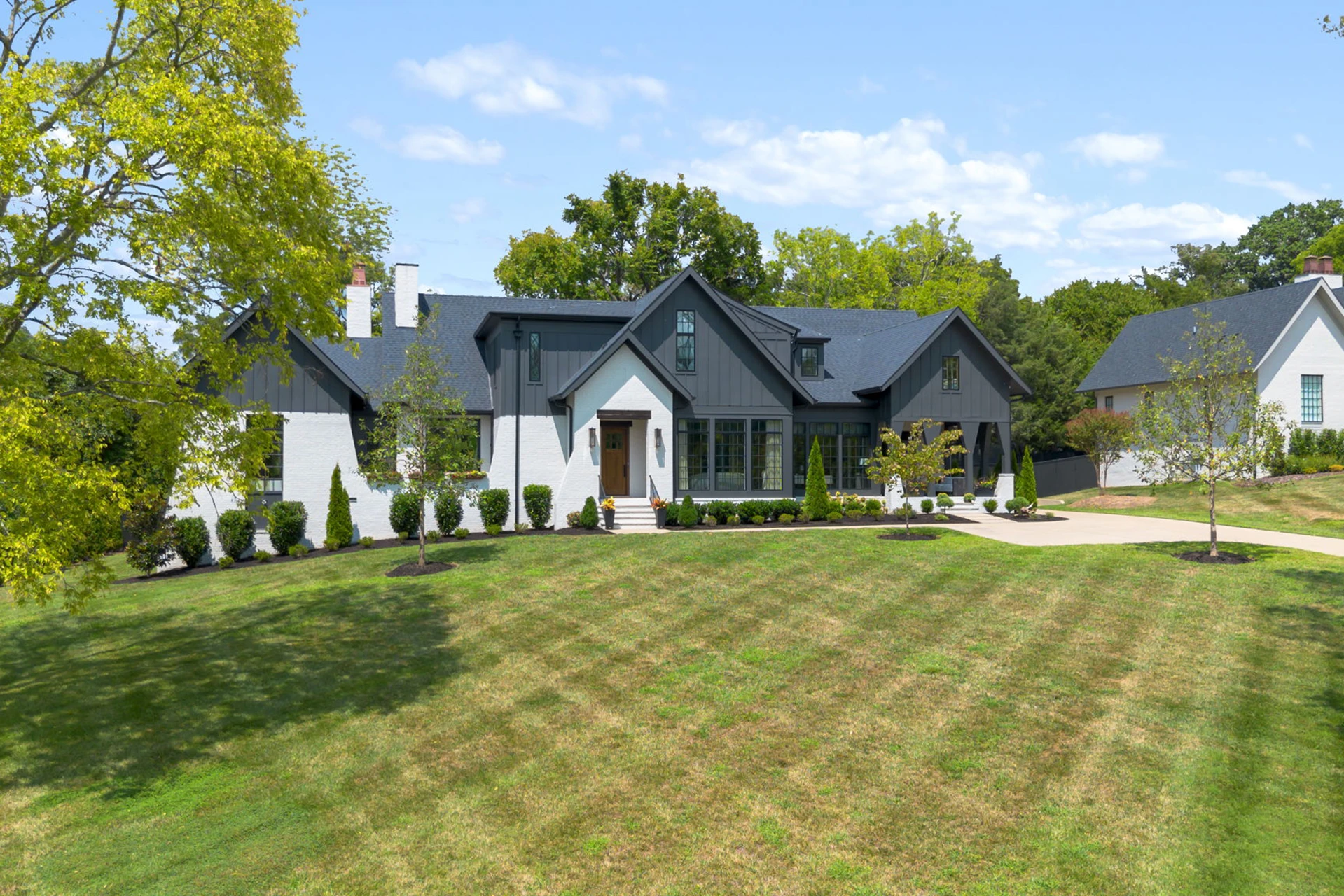 White and dark gray single-story modern farmhouse with black roof, multiple gables, and a wide green lawn