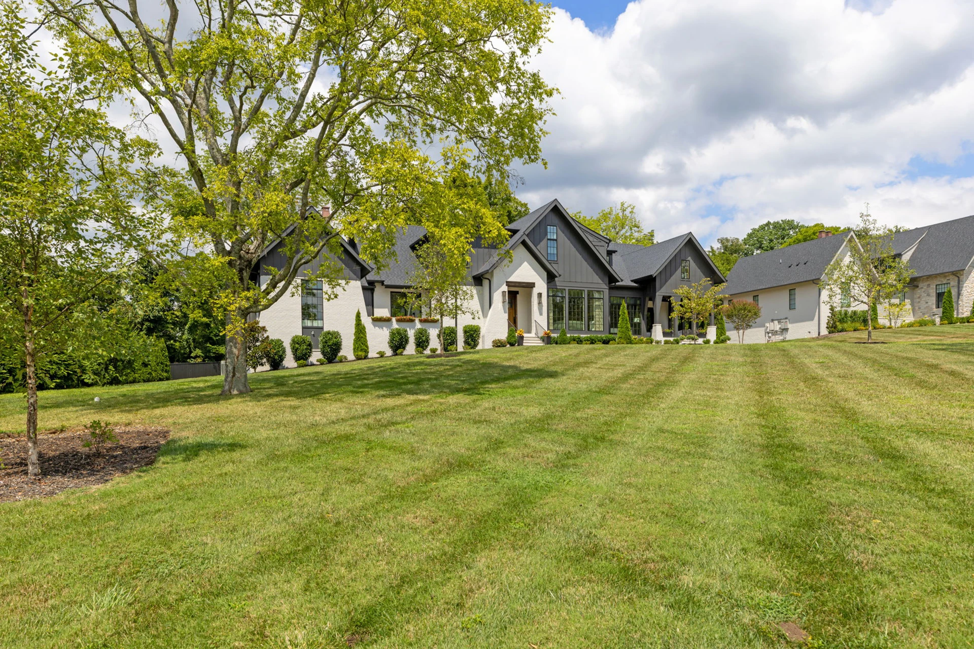 White and dark gray single-story home with black roof, a large shade tree, and an expansive lawn