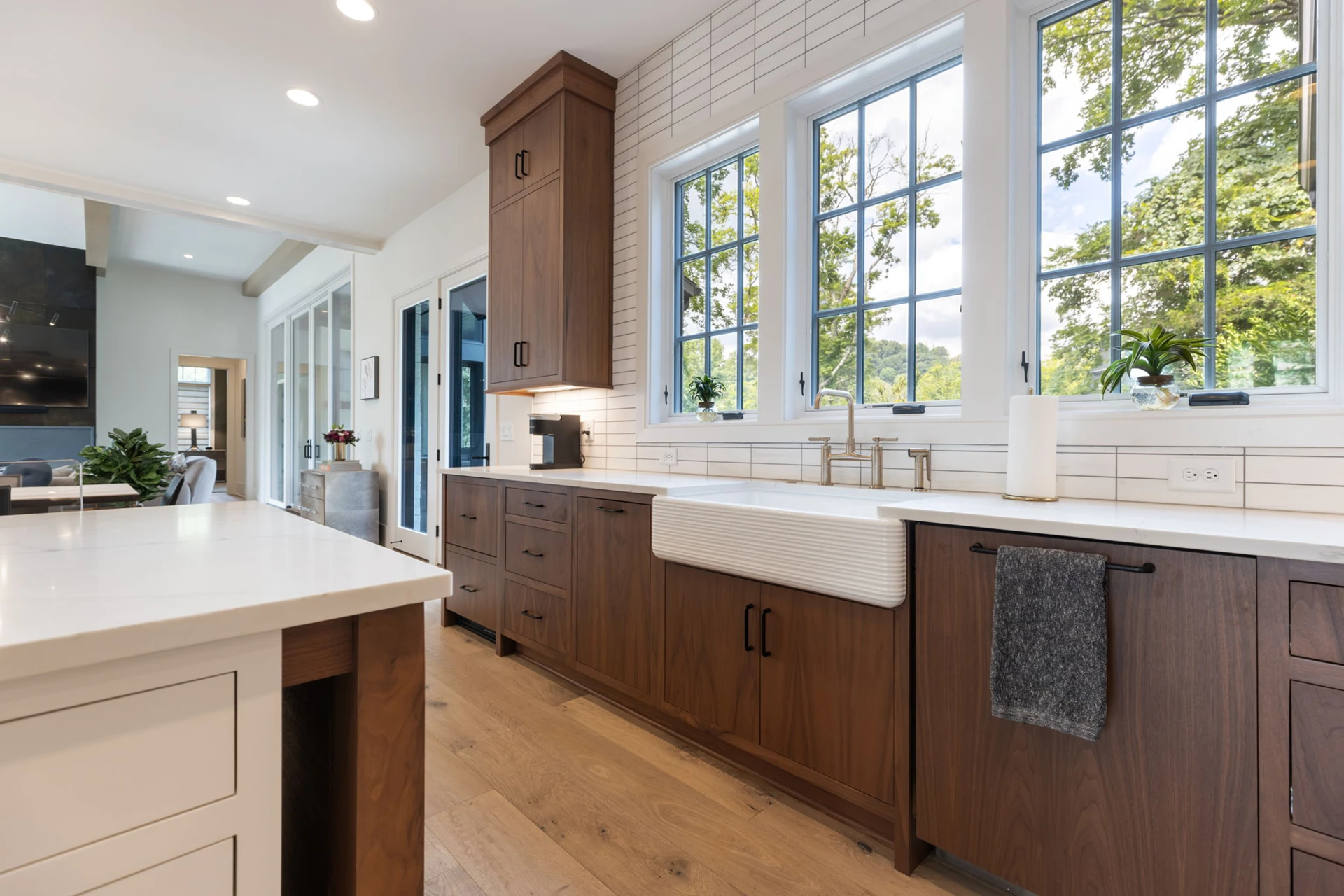 Kitchen with wood cabinets, white farmhouse apron sink, three large windows, and a white waterfall island