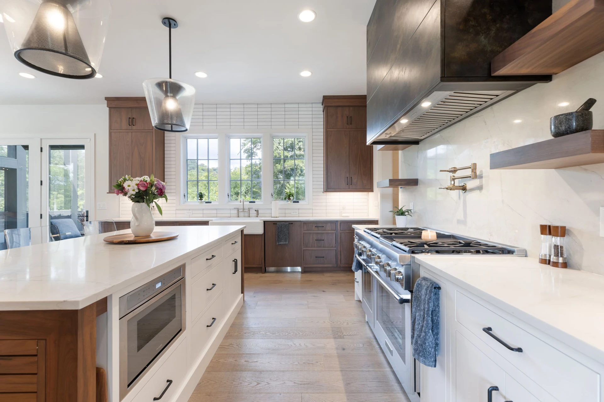 Kitchen with dark metallic hood, wood and white cabinets, waterfall island with built-in microwave, and farmhouse sink