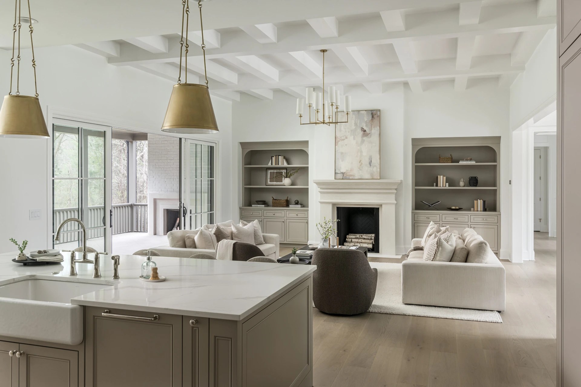 Open living and kitchen with vaulted beamed ceiling, marble island, and built-in shelving flanking a fireplace