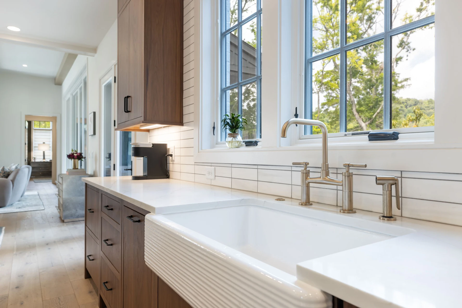 Prep kitchen corridor with wood cabinets, white farmhouse sink under black-grid windows, and brass faucet
